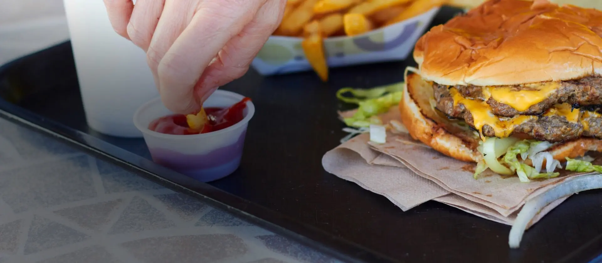 Close-up of a hand dipping fries in tomato sauce